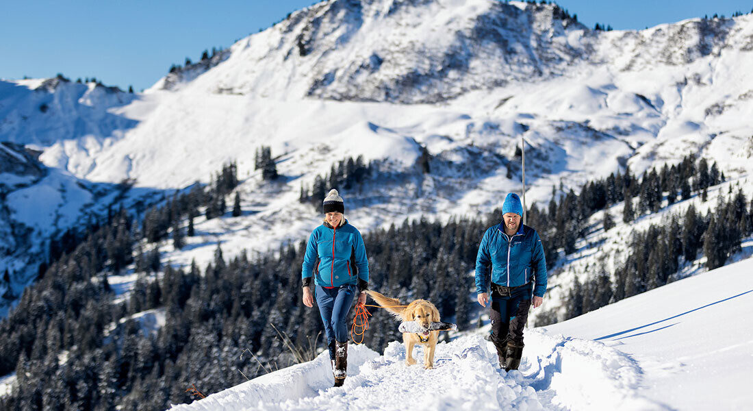 Die Gastgeber Peter und Silvia mit Hund Luke beim Spaziergang durch die verschneite Landschaft von Faschina.